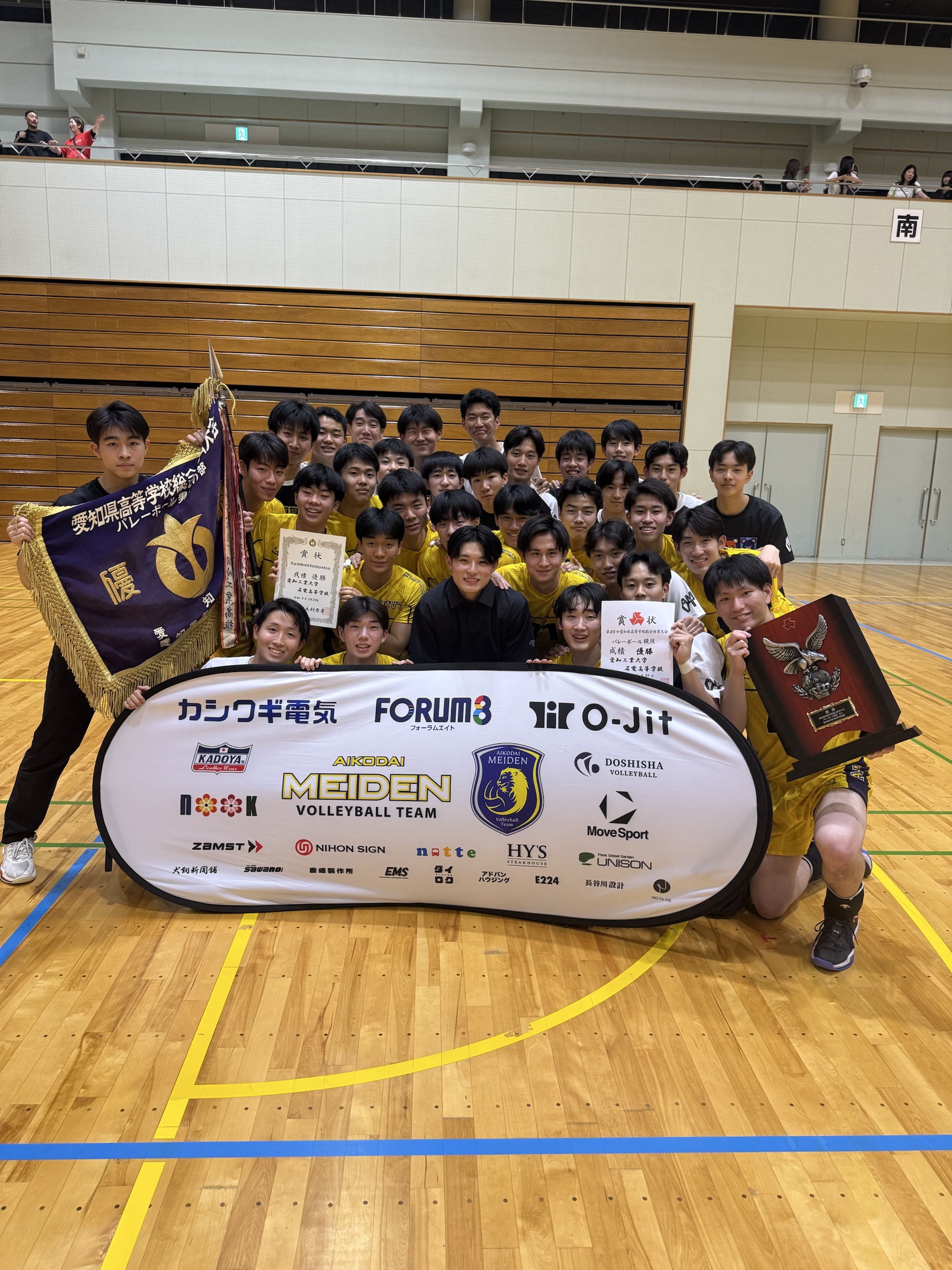 活動支援企業のロゴ幕を囲む愛工大名電男子バレー部